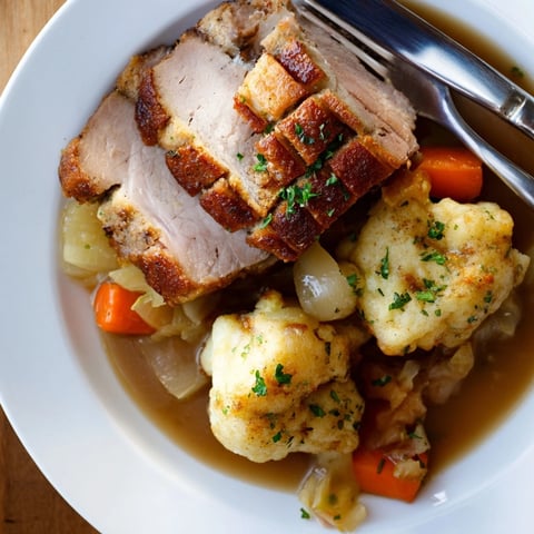 Zarter Schweinebraten mit knuspriger Kruste neben flaumigen Kartoffelknödeln und reichhaltiger Soße.