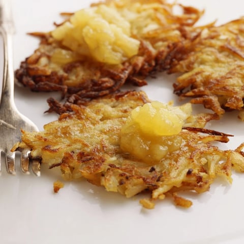 Goldene, knusprige Kartoffelpuffer mit süßer, hausgemachter Apfelsoße serviert.